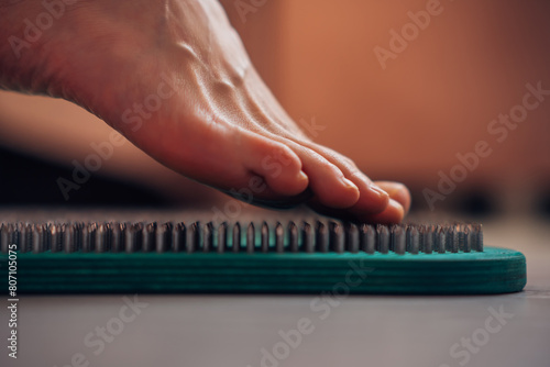 Woman try standing on Wooden Sadhu board with sharp nails, yoga desk for regular practice, relieves nervous stress, tiredness, emotional overexcitation close-up. Yoga Sadhu board for beginners