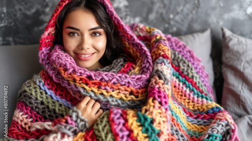   A woman sits on a couch, enveloped in a vibrant, multi-colored blanket She rests her hands on her hips, smiling directly at the camera photo