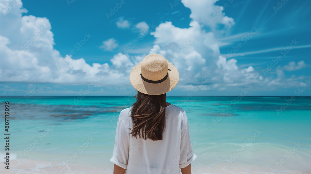 woman in white shirt and hat standing on beach, view from behind her back to ocean