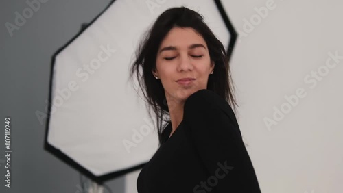 A young happy dark-haired woman is dancing in a photo studio.The woman touches her fluttering hair with her hands.