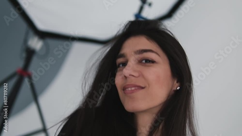 A young happy dark-haired woman is dancing in a photo studio.The woman touches her fluttering hair with her hands.