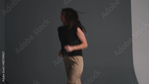 A young happy attractive dark-haired woman is dancing in a photo studio.