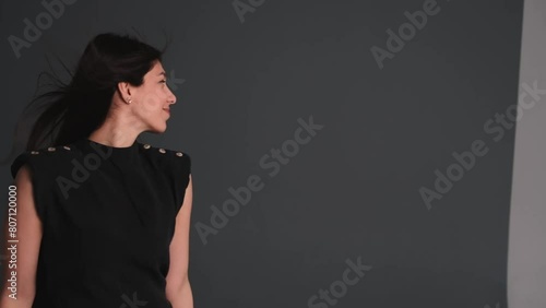 A young happy dark-haired woman is dancing in a photo studio.The woman touches her fluttering hair with her hands.
