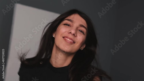 A young happy dark-haired woman is dancing in a photo studio.The woman touches her fluttering hair with her hands.