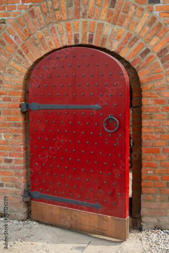 An old wooden door with a red handle in a brick wall.