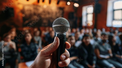 Close-up, hand with microphone ready to speak, blurred attendees of a classroom in the background, studio lighting isolates the subject photo