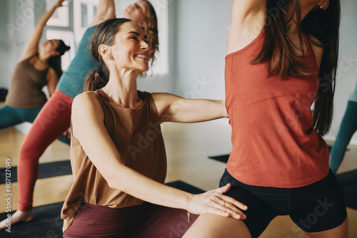 Young female yoga teacher smiling while helping her students with their poses during a class together in her studio photo