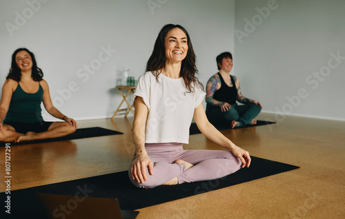 Female yoga teacher laughing while leading a group of students sitting on mats during a class on the floor of her studio photo