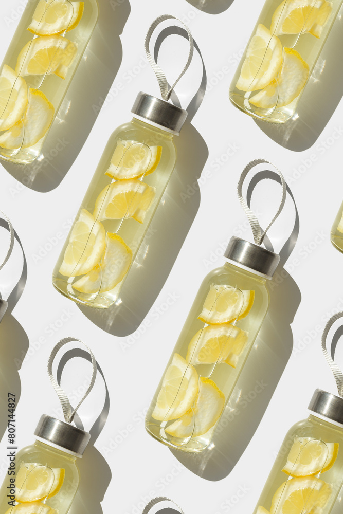 Top view glass bottles, water drink detox with lemon at sunlight on white background, geometric non-seamless pattern. Infused water with slices citrus fruit. Minimal style photo with health drinks Top view glass bottles, water drink detox with lemon at sunlight on white background, geometric non-seamless pattern. Infused water with slices citrus fruit. Minimal style photo with health drinks