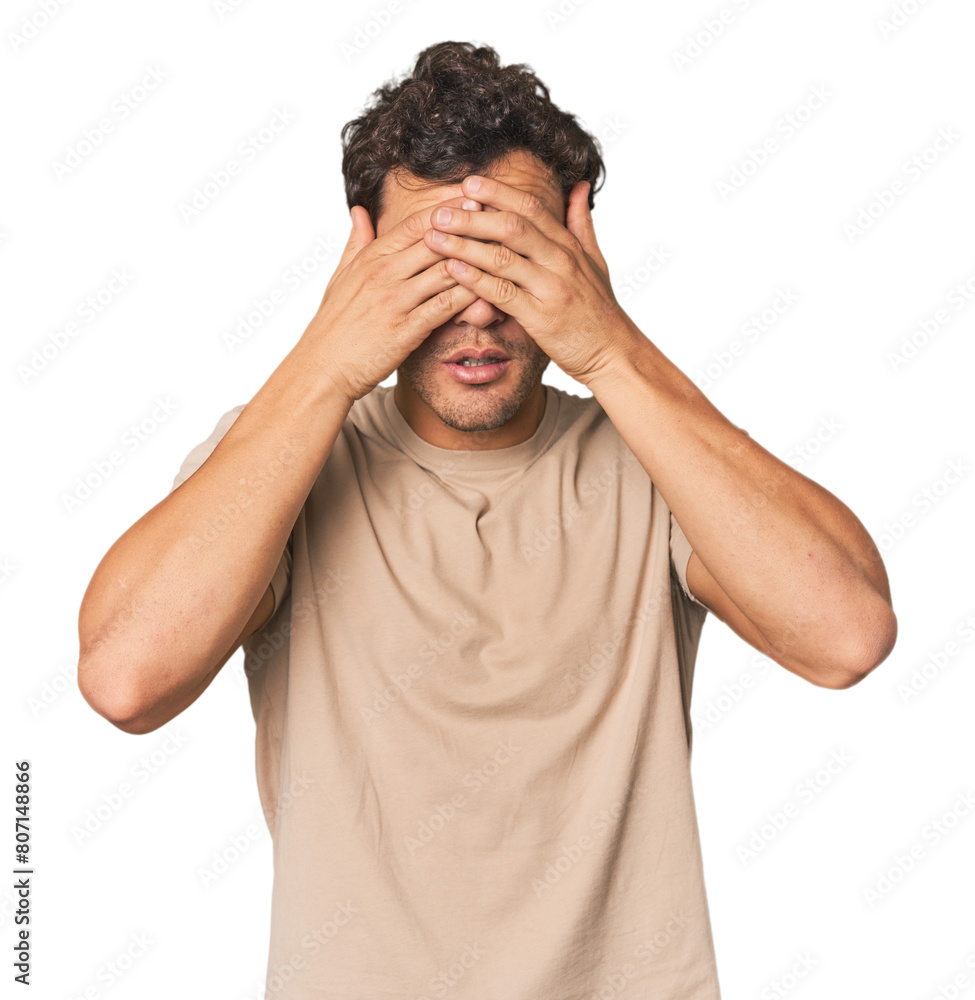 Young Hispanic man in studio afraid covering eyes with hands. Young Hispanic man in studio afraid covering eyes with hands.