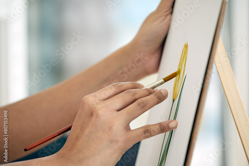 Close-up view, the artist's hand delicately holds brush to paint yellow tulip flower on canvas paper