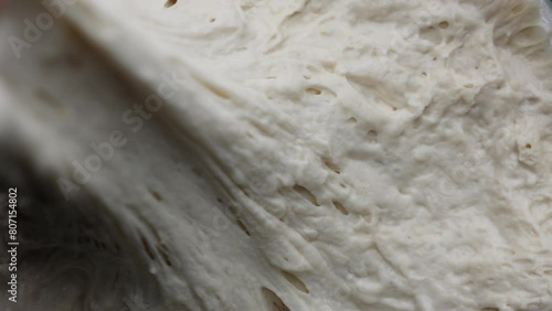 hand stretching and pulling dough (shaping a loaf of bread manually in bakery) cooking baking yeast water flour, sticky stretchy gluten dough photo