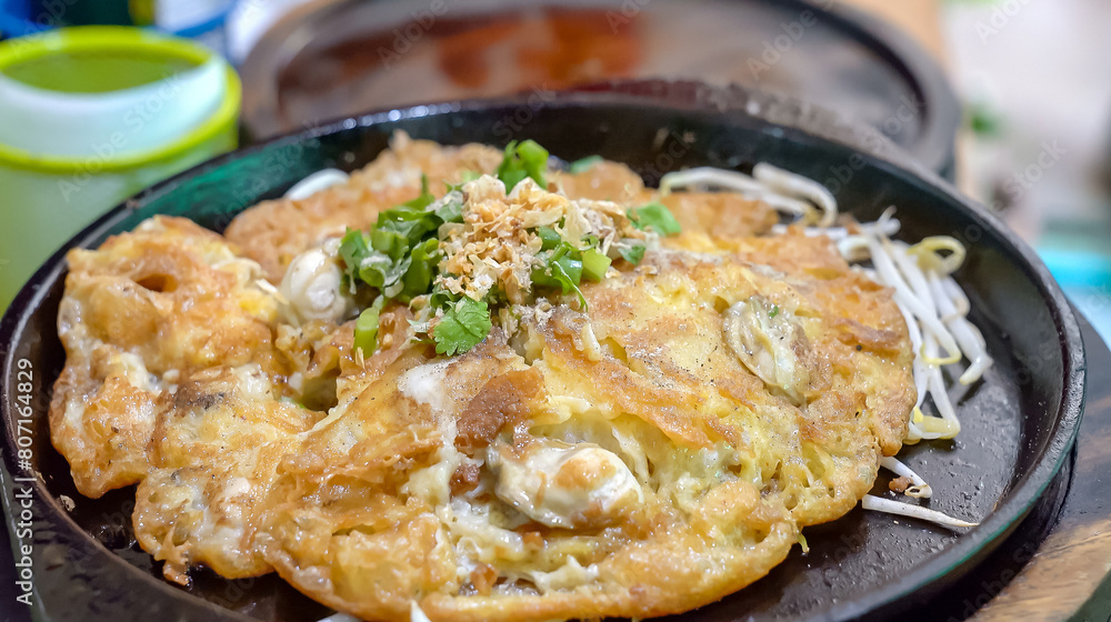 On a hot, black pan, a pan fried oyster omelet with bean sprouts. In the hot pan, this menu is ready to be served and consumed. On a hot, black pan, a pan fried oyster omelet with bean sprouts. In the hot pan, this menu is ready to be served and consumed.