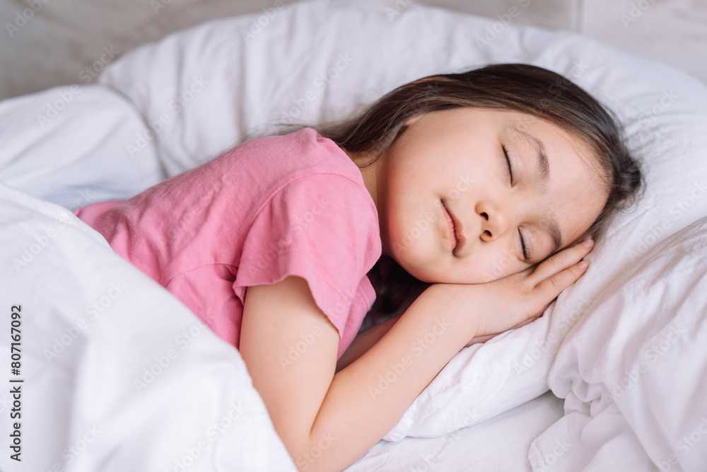 Little girl in pink pajamas sleeps in a white bed. Little girl in pink pajamas sleeps in a white bed.
