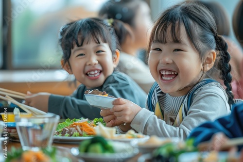 Two Asian elementary school students joyfully sharing a meal together, their faces beaming with happiness and laughter photo