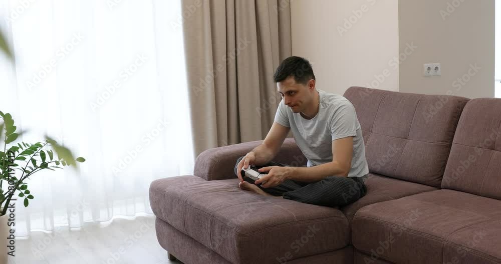 man playing video games while sitting on couch in living room, gamer use a joystick on console man playing video games while sitting on couch in living room, gamer use a joystick on console