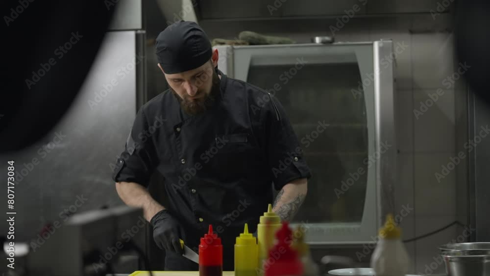 Side view of a confident male chef in a black uniform wearing black rubber gloves preparing a salad and cutting vegetables in the kitchen in a restaurant Side view of a confident male chef in a black uniform wearing black rubber gloves preparing a salad and cutting vegetables in the kitchen in a restaurant