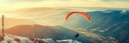 An adventurous paraglider soars majestically over a breathtaking mountain range with a sunset backdrop