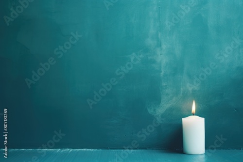 Teal background with white thin wax candle with a small lit flame for funeral grief death dead sad emotion with copy space texture for display products 