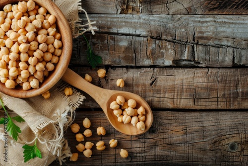 Top view of wooden bowl and spoon with chickpeas on wooden surface