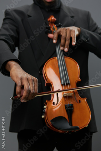 Elegant African American man playing violin in tuxedo on gray background in classical music performance concept