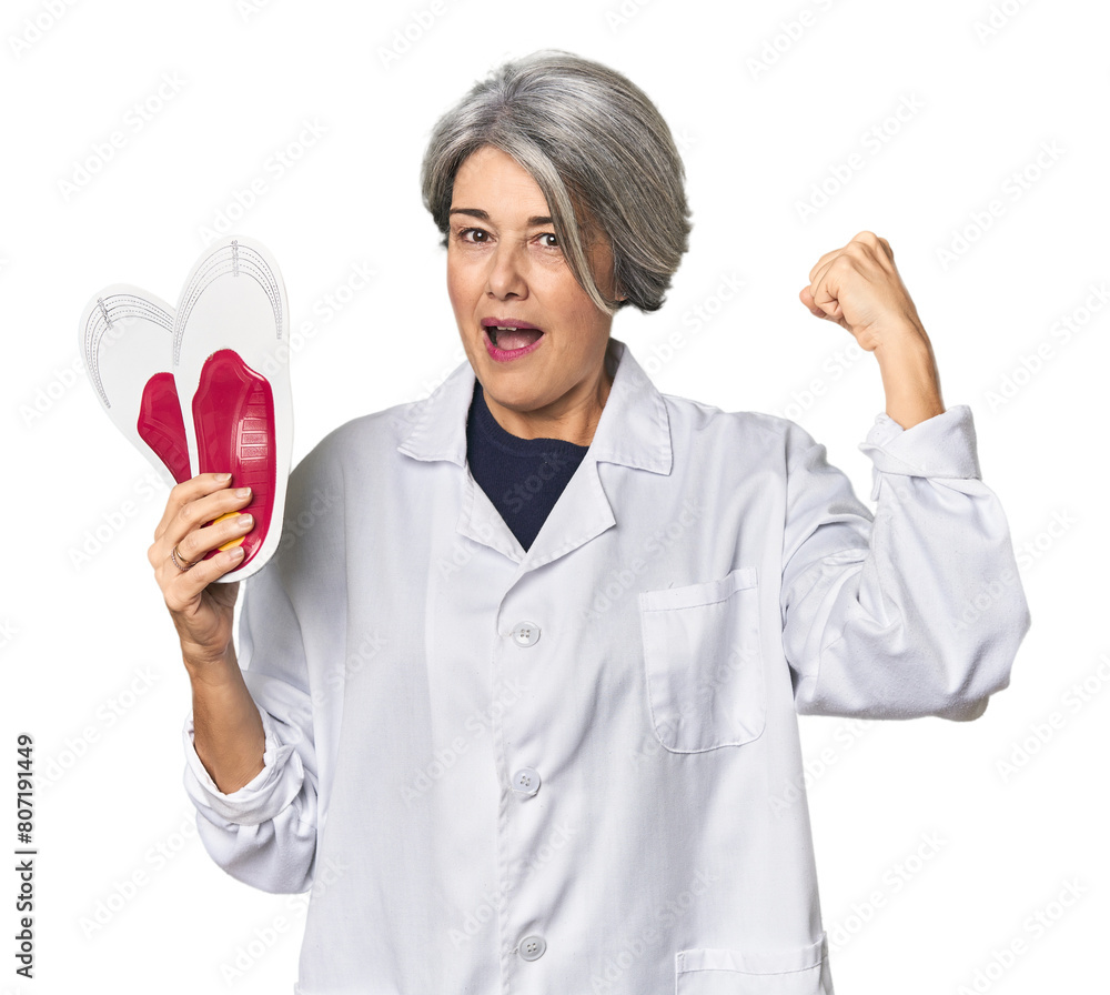 Caucasian mid-age female podiatrist holding insole raising fist after a victory, winner concept. Caucasian mid-age female podiatrist holding insole raising fist after a victory, winner concept.