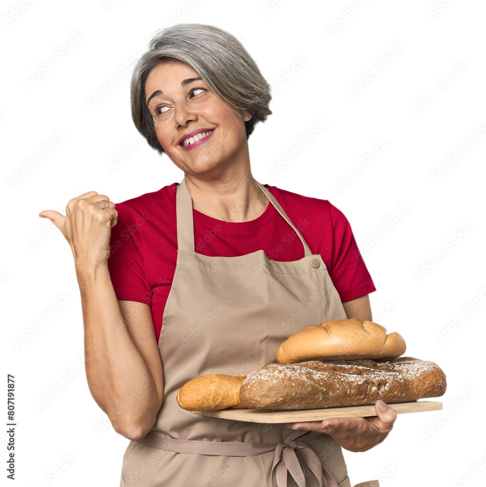 Caucasian mid-age baker with bread loaves points with thumb finger away, laughing and carefree.