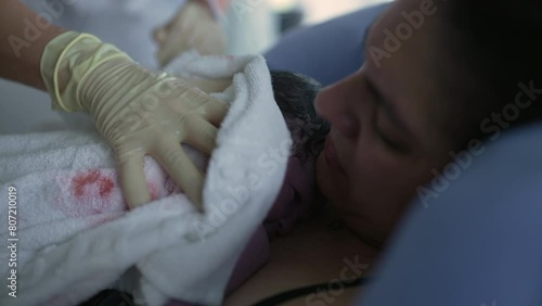 Nurse's hand trying to make newborn baby cry right after birth, infant's first seconds of life resting on mother's chest during childbirth moment, birthing of new life