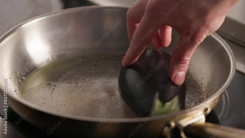 Influential head cook placing slice of eggplant into stainless steel frying pan. Yellow oil heating on surface and absorbed into vegetable. Process of creating tasty dish.