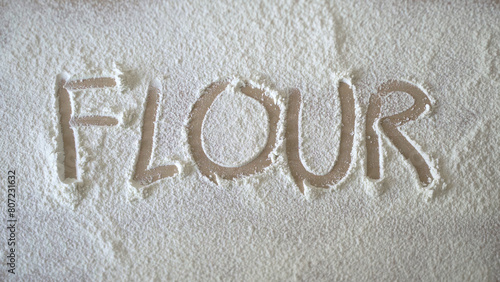 Flour written on wooden table with finger over dusted flour