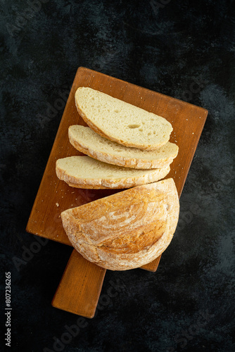 Fresh slice of bread on wooden cutting board on the black background.