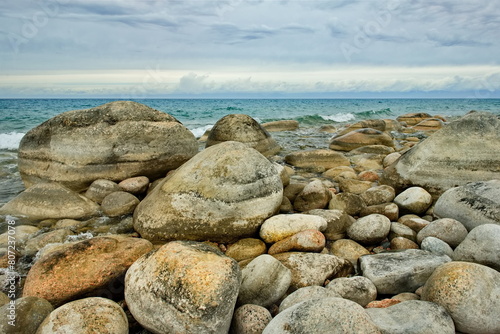 Northern Kyrgyzstan. The landscape of the cold Issyk-Kul lake with colored rounded stones of various sizes along the picturesque shore.