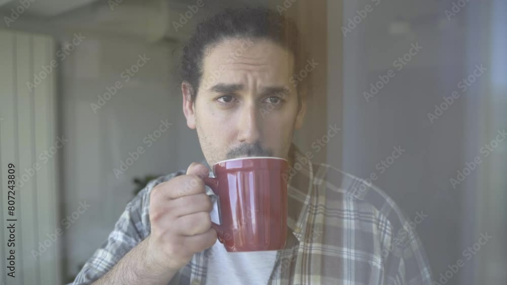 Positive thinking. Depressed young male looks through window while drinking tea Positive thinking. Depressed young male looks through window while drinking tea