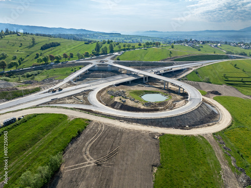 New fragment of highway under construction on Zakopianka road, Poland, clearing Nowy Targ town. Entrance and exit ramps, traffic circle. State in May 2024. Aerial view. Old road in the background
