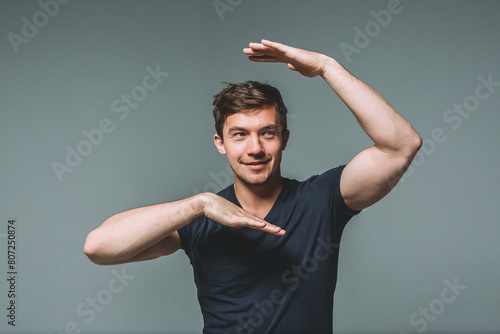 Waist portrait of a young handsome man with a muscular build on a gray background. A man dances, depicts a tectonic dance or waacking dance with his hands photo