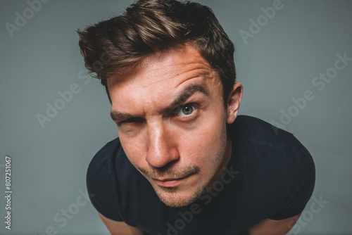 Close-up of a man's face on a gray background. Emotion: What are you doing here? I can see everything. I'm watching you. Are you sure? One eyebrow is raised