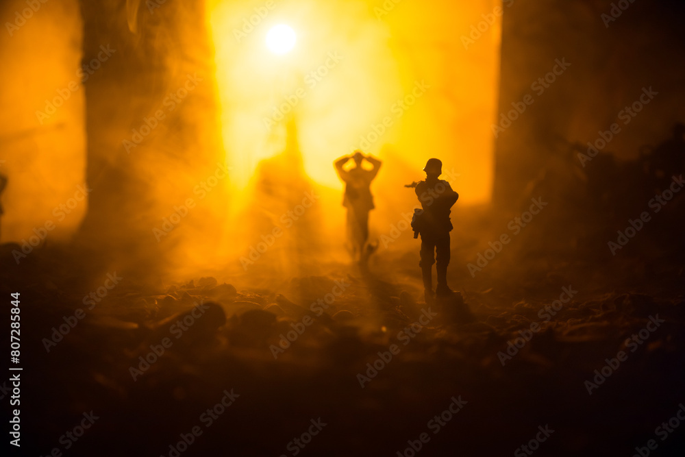 Fototapeta premium Military silhouettes fighting scene on war fog sky background. A German soldiers raised arms to surrender. Plastic toy soldiers with guns taking prisoner the enemy soldier.