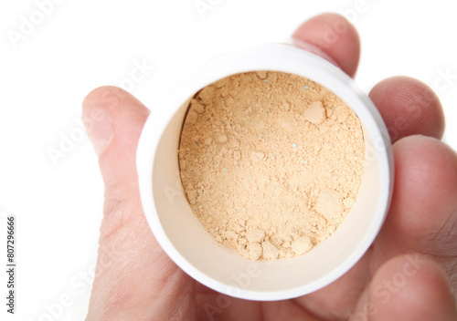 Styptic powder container held by hand. Yellow powder in plastic container. Pet first aid product to stop dog nail or cat claw injury from cutting. For veterinary use. Selective focus. White background