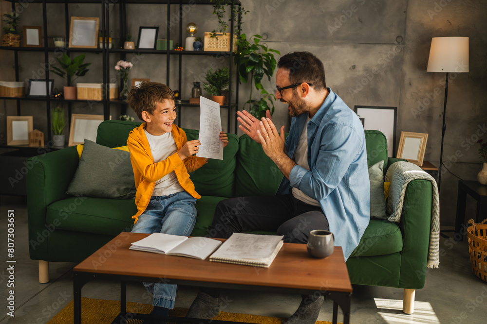 Happy and satisfied little boy show his father good grade on his test Happy and satisfied little boy show his father good grade on his test