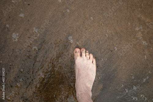a man's foot on the sand washed by water