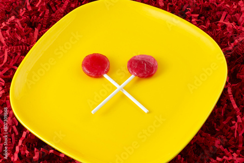 Two cherry lolllipops on yellow snack plate on background of crinkled shredded paper
