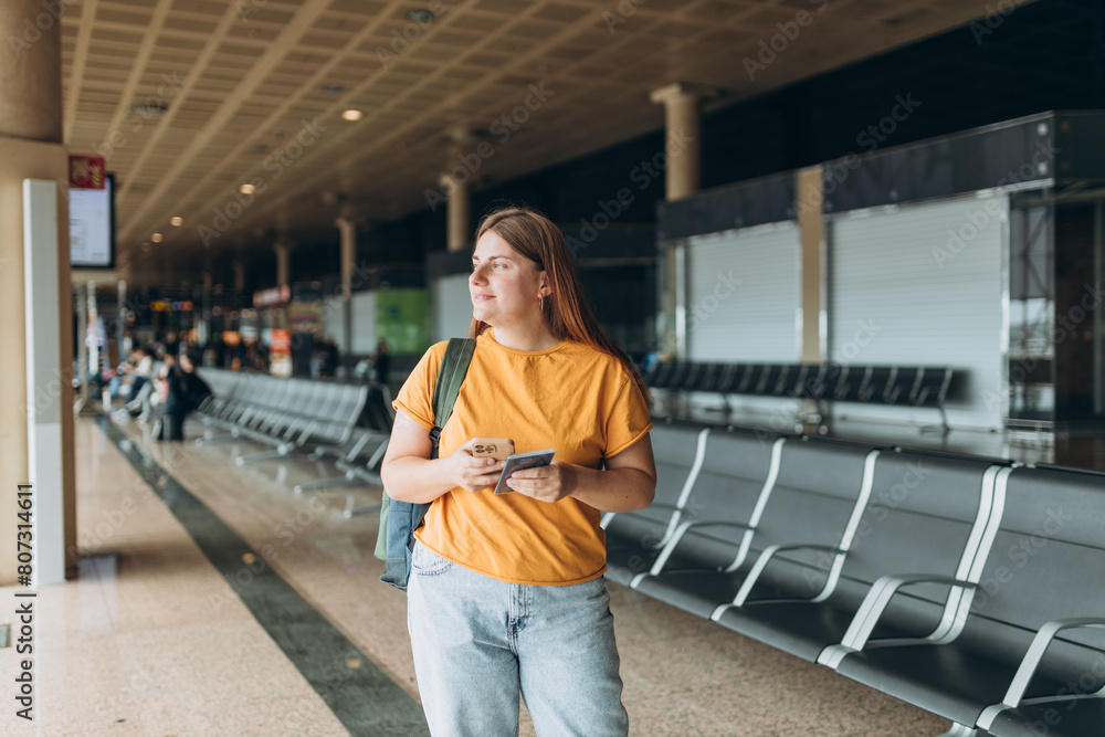 Fototapeta premium Happy Caucasian Woman waiting at Flight Gates for Plane Boarding, Uses Mobile Smartphone. 30s female Checking Trip Destination on Internet, concept of traveling