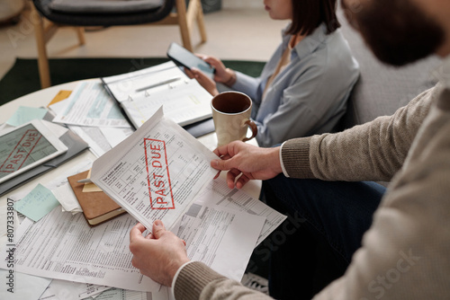 Hands of young unrecognizable man holding final notice bill with past due stamp over table with unpaid financial documents