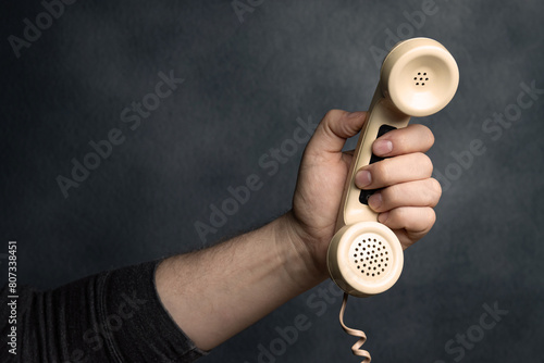 Hand reaching out with landline telephone receiver.