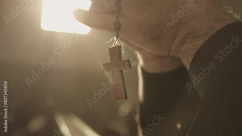 Christian rosary with cross hanging from male hands and swinging close up. Monk holding prayer beads in clasped arms while praying in cathedral closeup. Christianity concept