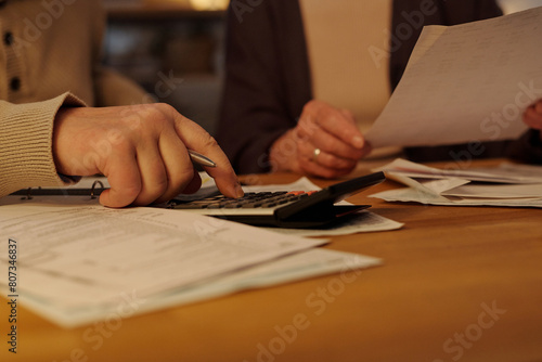 Hand of senior unrecognizable man pressing button of calculator while sitting by table with financial bills and checking sums
