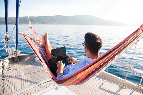 Working in sea traveling. Man with laptop in beach hammock. Summer vacation, living on yacht. Successful freelancer using computer. Workplace on nature outdoors, home office. Business lifestyle
