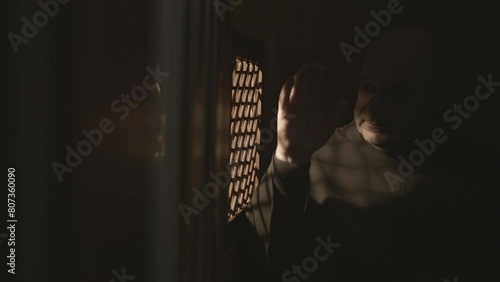 Christian monk in dark confessional booth, crossing and talking medium shot. Monastery clergyman listening to confession through window. Forgiveness concept photo