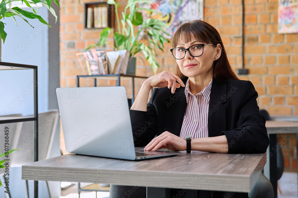 Middle-aged business woman working remotely with laptop in coworking Middle-aged business woman working remotely with laptop in coworking