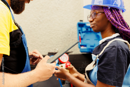 Seasoned mechanic coworkers refilling freon and repairing leaks in outdoor hvac system. Knowleadgeable engineers diagnosing air conditioner to prevent refrigerant loss and ensure optimal performance photo